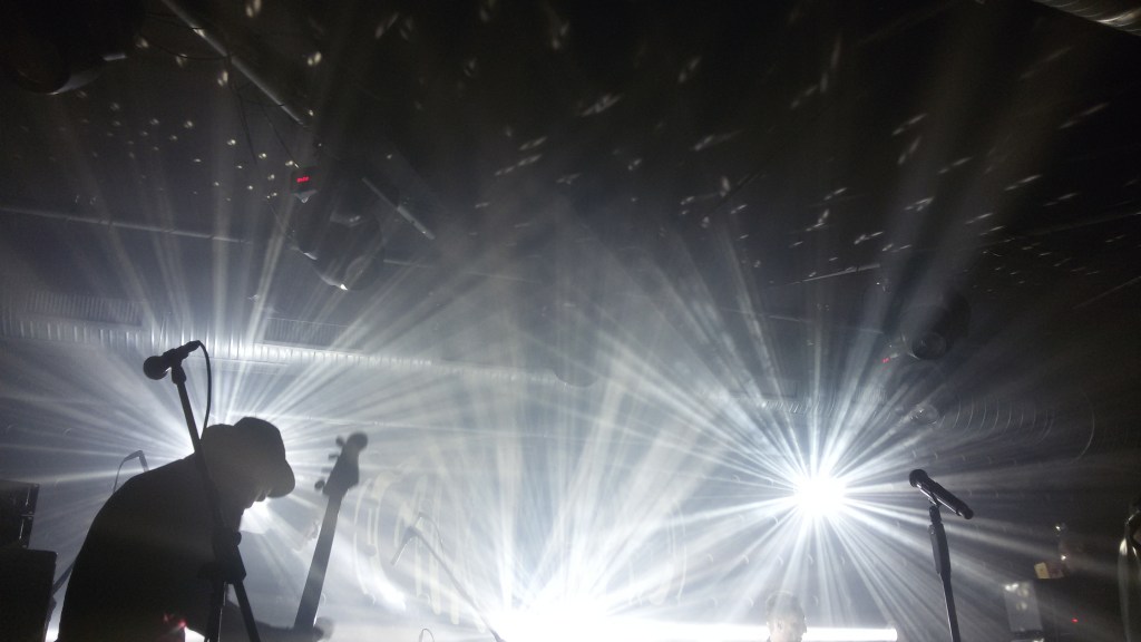 A musician on stage with a guitar and blinding lights behind.
