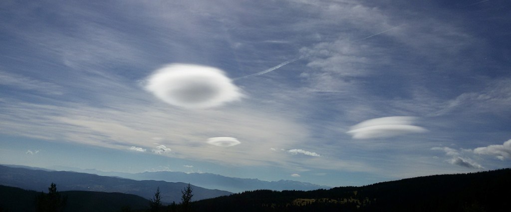 Clouds that look like flying saucers over mountain tops.