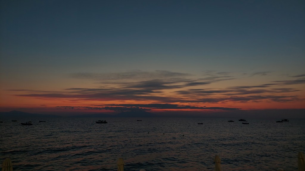 a sunset over see with boats